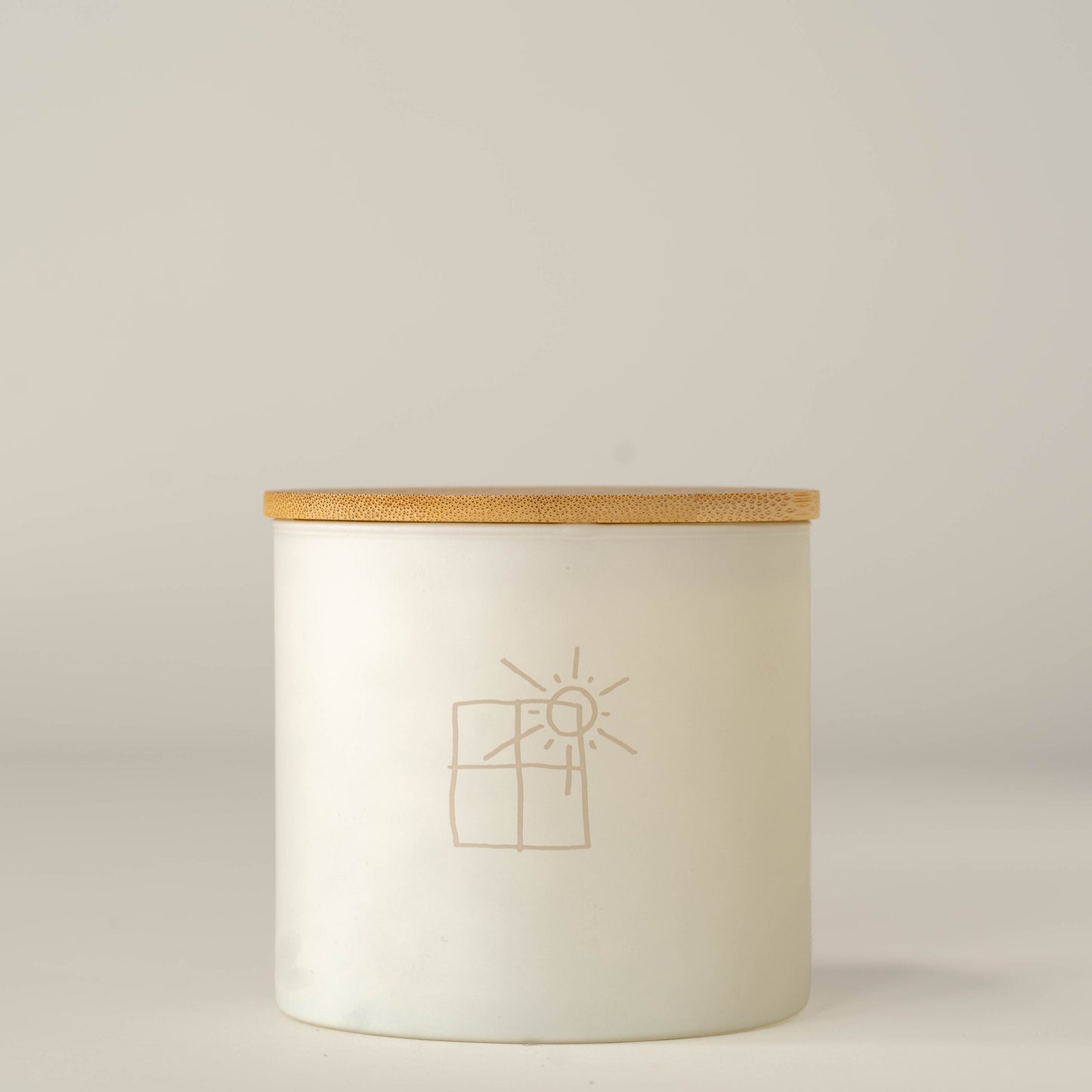 A white glass jar candle with a light natural wood lid, featuring a minimalist beige line drawing of a sun and window on the front, set against a neutral light gray background.